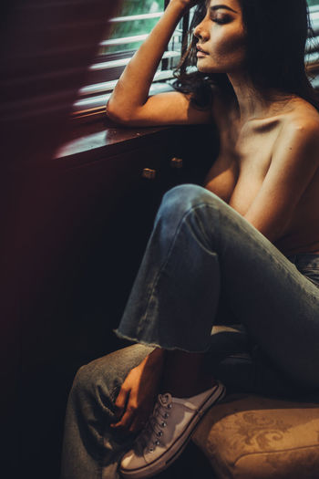 Shirtless woman sitting on chair by window at home