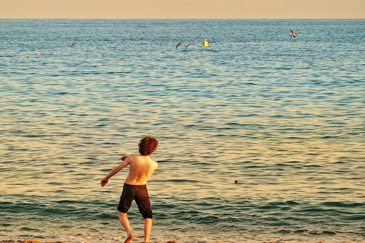 Shirtless teenage boy running towards sea at beach