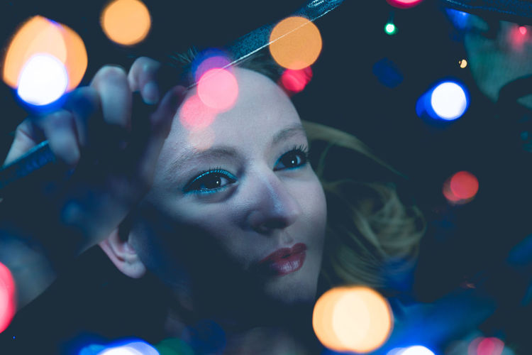Close-up of young woman with colorful illuminated lights in darkroom