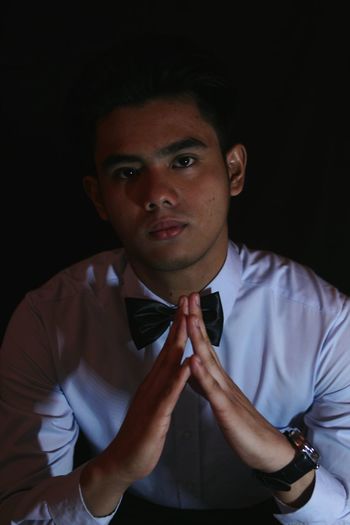 Portrait of young man joining hands against black background