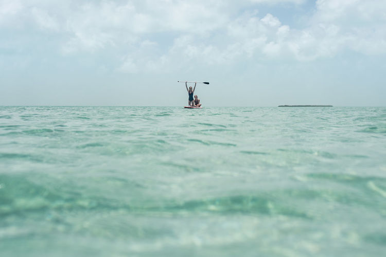Friends paddleboarding in sea against sky