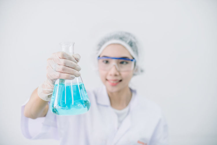 Scientist holding beaker with blue liquid standing against white background