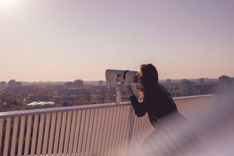 Side view of woman looking through coin-operated binoculars while standing on observation point