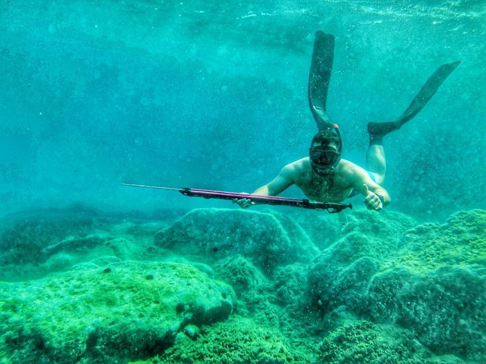 Shirtless man holding harpoon swimming undersea