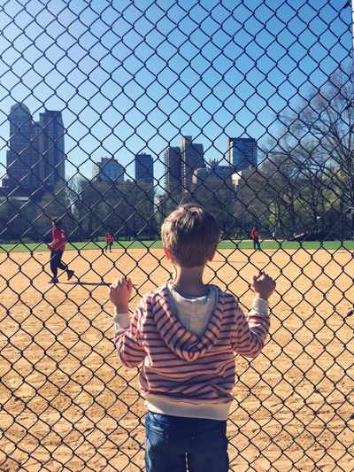 Rear view of boy looking through chainlink fence at central park