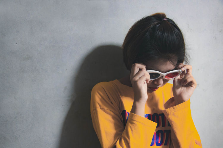 Woman wearing sunglasses against wall