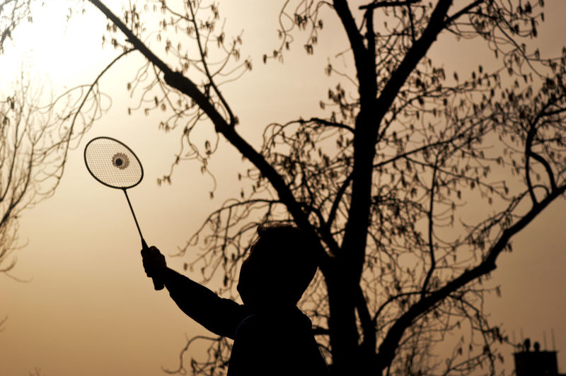 Silhouette man playing badminton during sunset
