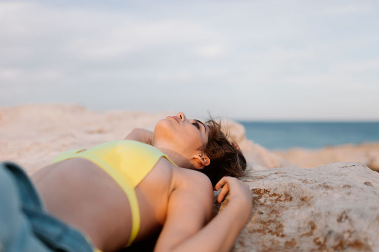 Woman lying on beach against sky