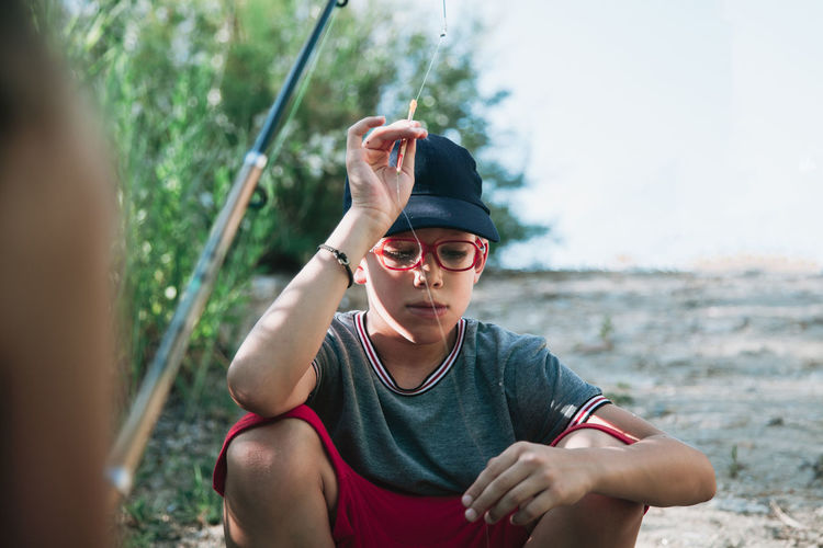Boy holding fishing rod while crouching on field