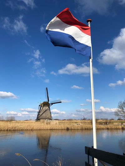 Low angle view of netherlands flag on lake against sky with windmill background