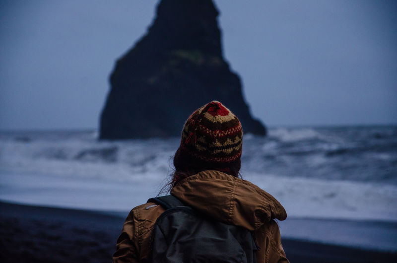 Rear view of woman with backpack looking at sea view during dusk