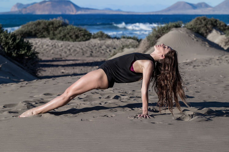 Full length of woman practicing yoga at beach against sky