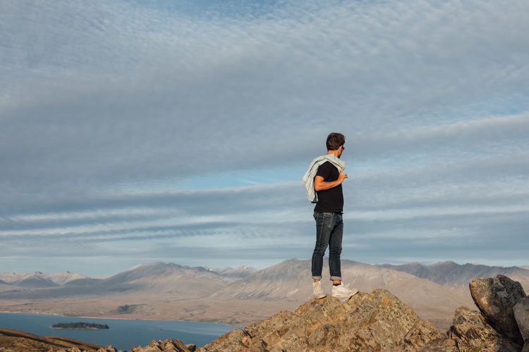 Full length of man standing on cliff against cloudy sky