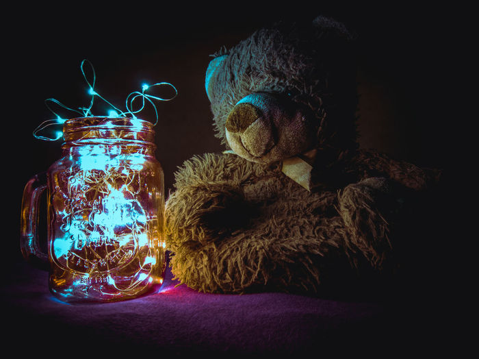 Stuffed toy by illuminated jar against black background