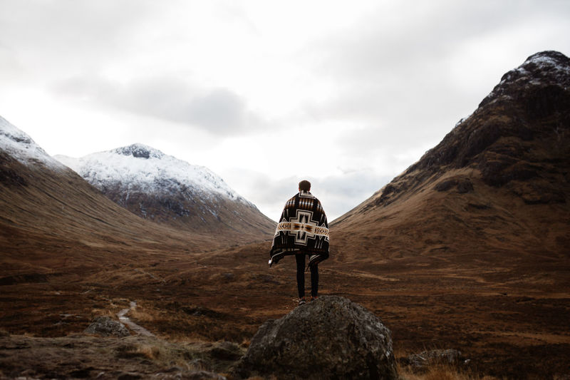 Back view of unrecognizable male explorer standing on rock and enjoying scenery of mountains in fall in scottish highlands