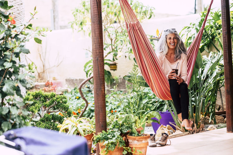 Smiling woman sitting on hammock by plants