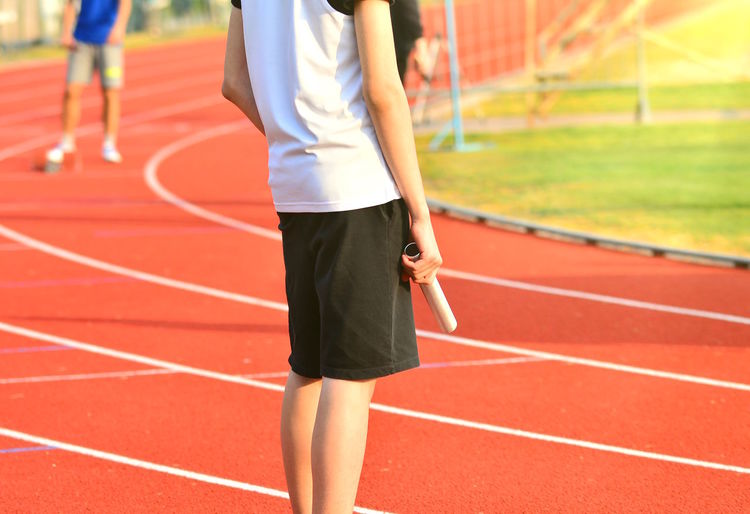 Midsection of athlete holding relay baton while standing on starting line