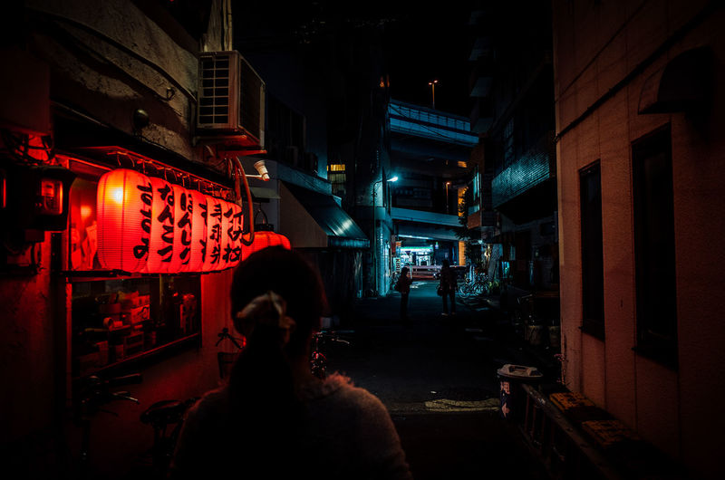 Rear view of woman walking on alley by illuminated japanese lanterns in city at night