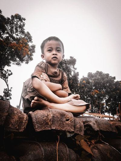 Portrait of cute boy sitting on rock against sky