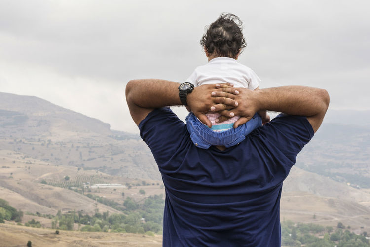 Rear view of father carrying son on shoulder against mountains