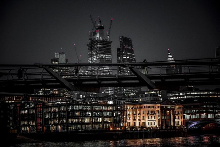 Illuminated bridge over river and buildings against sky at night