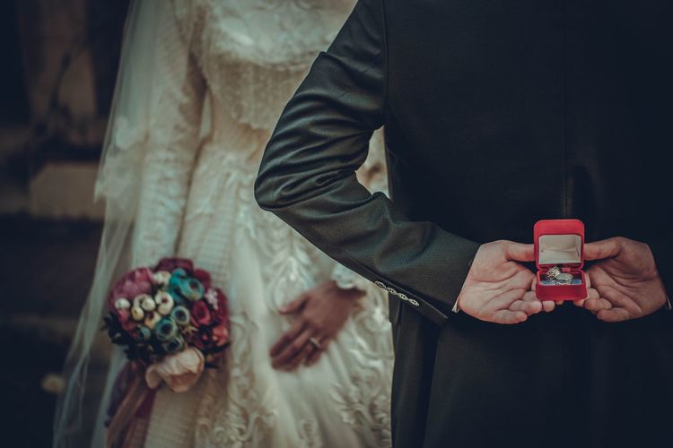 Midsection of groom hiding ring box with bride during wedding ceremony
