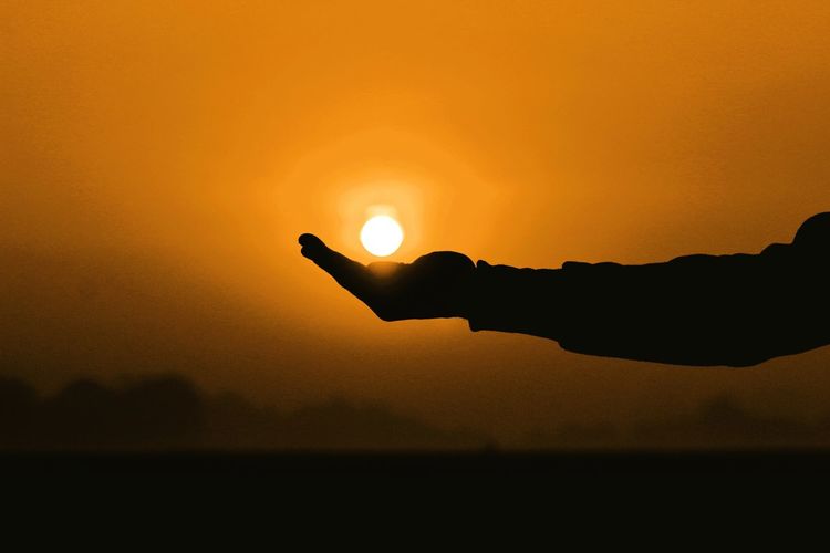 Silhouette hand against sky during sunset