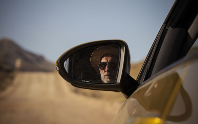 Adult man in sunglasses on side view mirror of car on dirt road