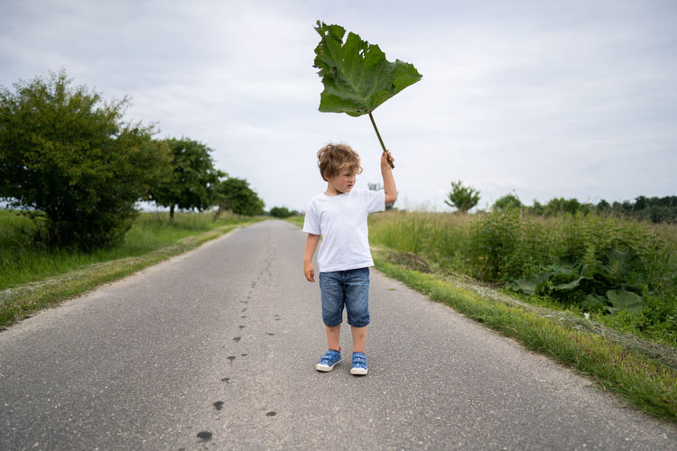 Rear view of boy standing on road against sky