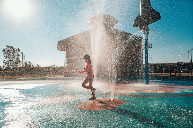 Full length of boy splashing water against sky