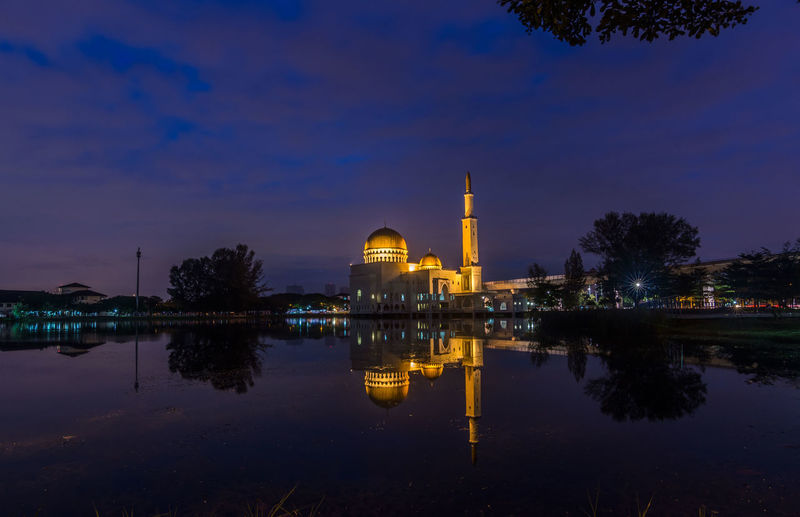 Reflection of illuminated mosque in lake against sky
