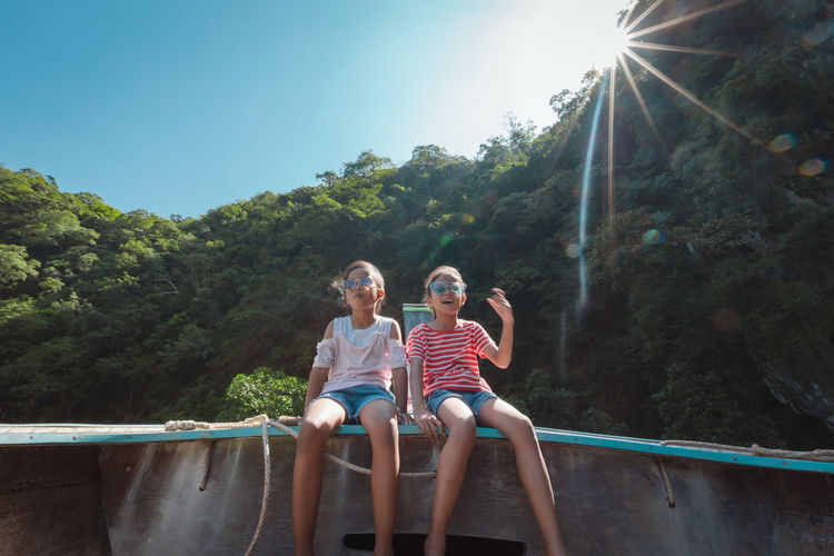 Low angle view of girls sitting against forest