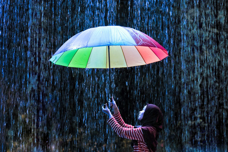 Teenage girl holding multi colored umbrella against rain