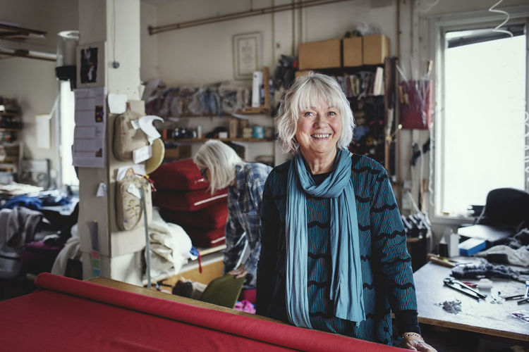 Portrait of smiling senior female standing at workbench in workshop