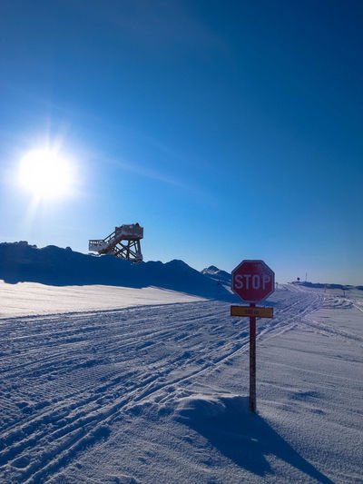 Stop sign on snow covered field against clear blue sky