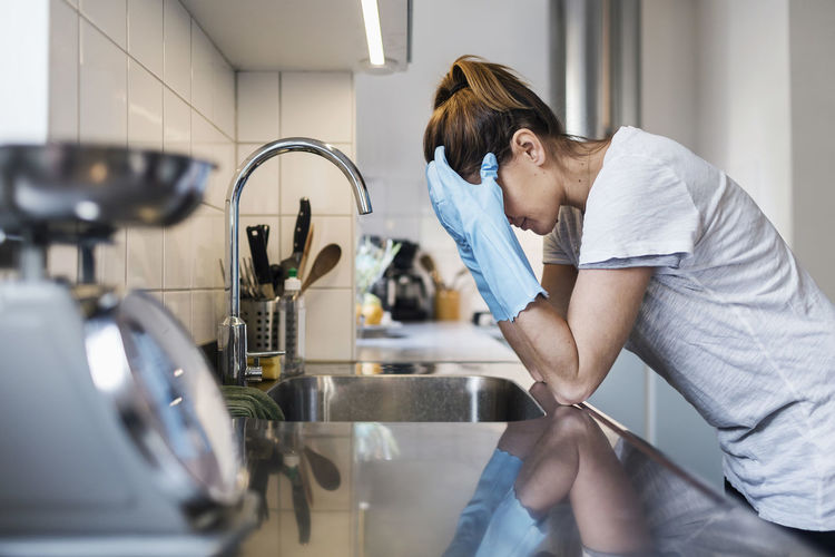 Side view of tensed woman leaning at sink in kitchen