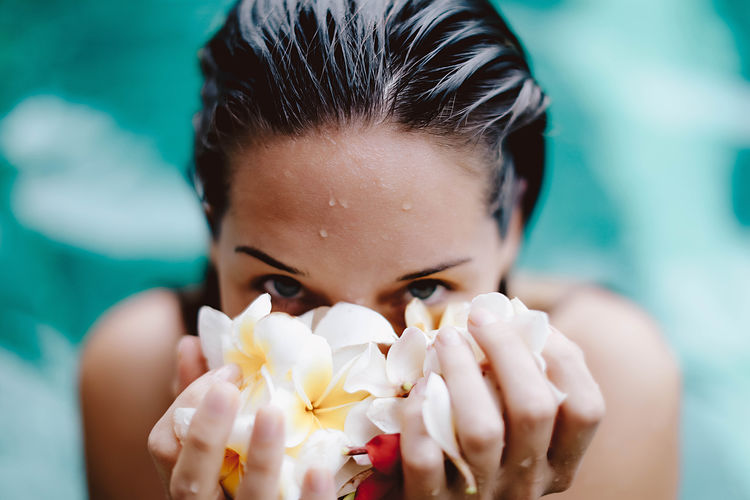 Blurred close up portrait of the young girl with wet hair holding balinese flowers