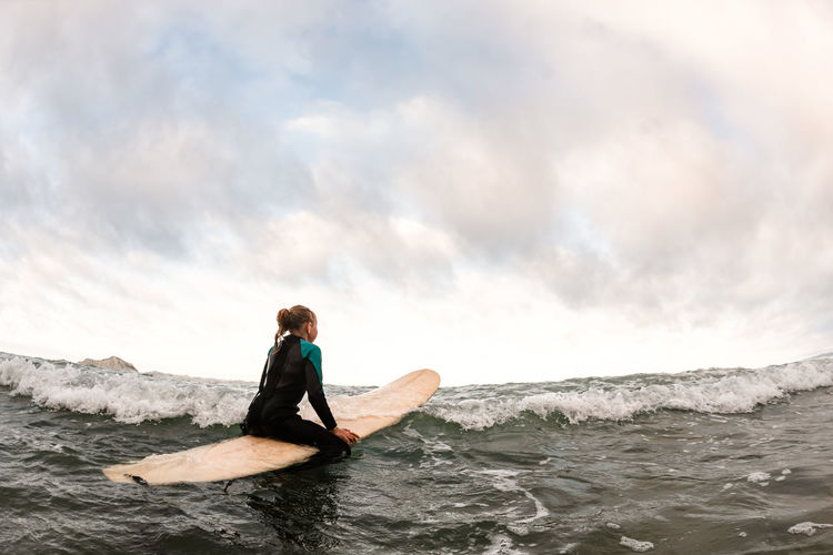 Adolescent girl looking away sitting on a surfboard in the ocean