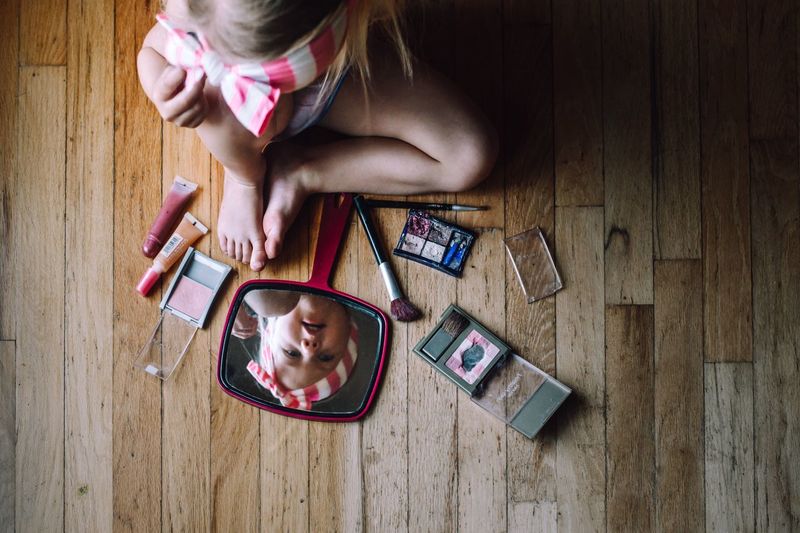 Directly above shot of girl playing with beauty products on hardwood floor