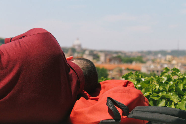 Rear view of man sleeping on backpack against sky