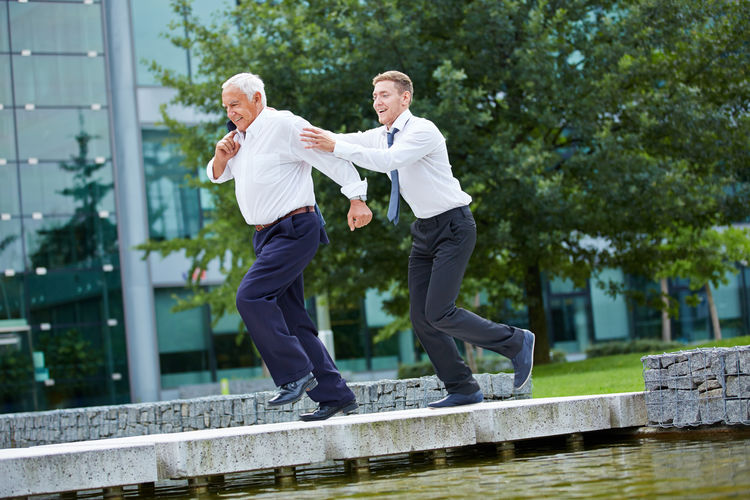 Happy colleagues walking on retaining wall over lake