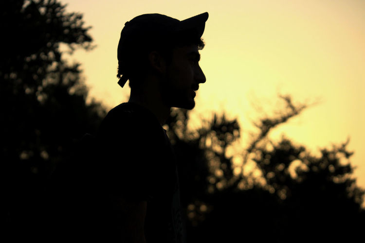 Side view of silhouette teenage boy standing against sky during sunset