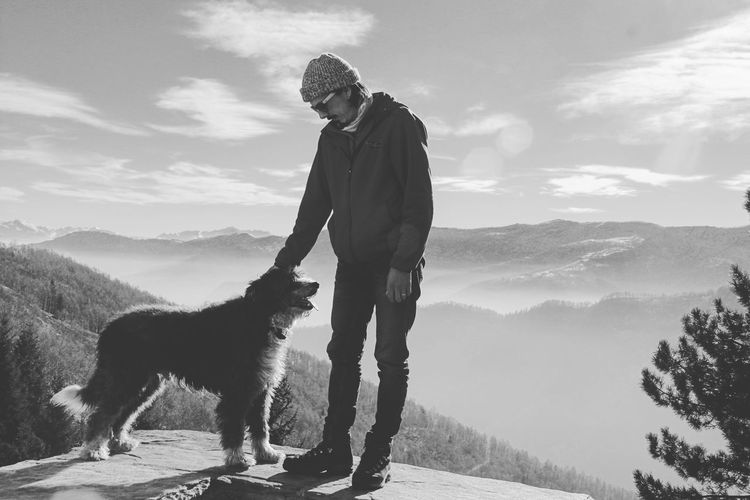 Man with dog standing on mountain against sky