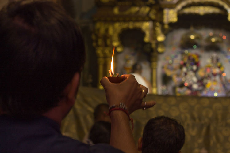 Rear view of man holding lit diya against idols in temple