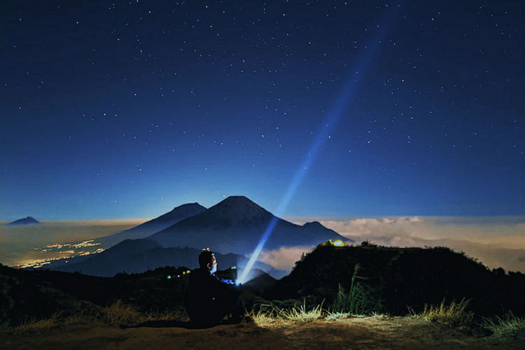 Silhouette man sitting on land against sky at night