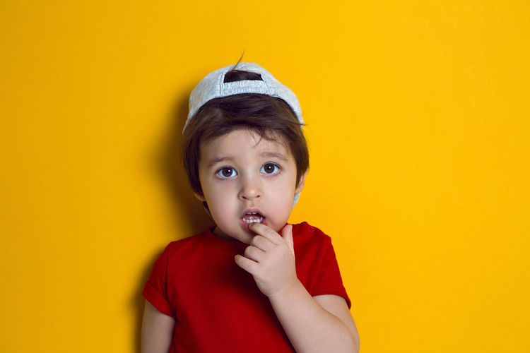 Cheerful baby boy in red t-shirt stands on yellow background