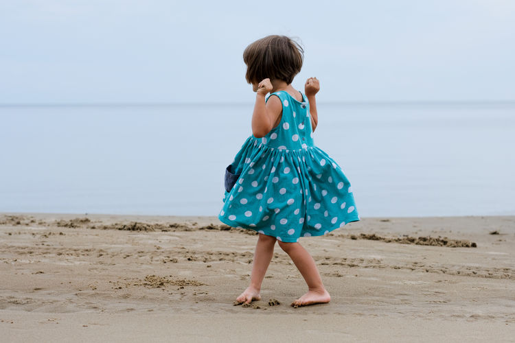 Toddler girl in a tourqouise polka-dot dress playing at the beach 