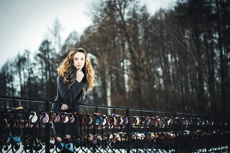 Portrait of beautiful woman with hand on chin leaning on railing with love locks