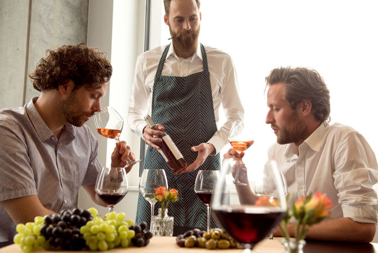 Bartender looking at customers tasting wine while sitting at table in room