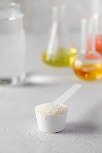A scoop with hydrolyzed collagen powder against the background of laboratory flasks. food additives,